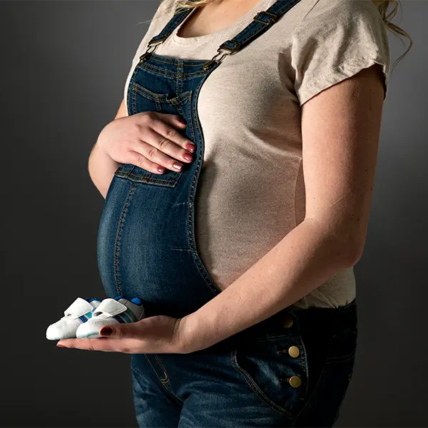Detailaufnahme beim Babybauch Shooting in Zofingen mit kleinen Babyschuhen, Jeanslatzhose und ruhiger Studioatmosphäre