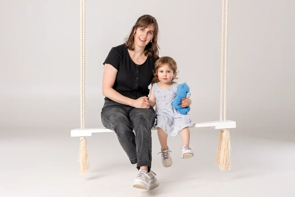Natürliches Familienfoto in Zofingen mit Mutter und Kleinkind auf einer weissen Schaukel im Fotostudio