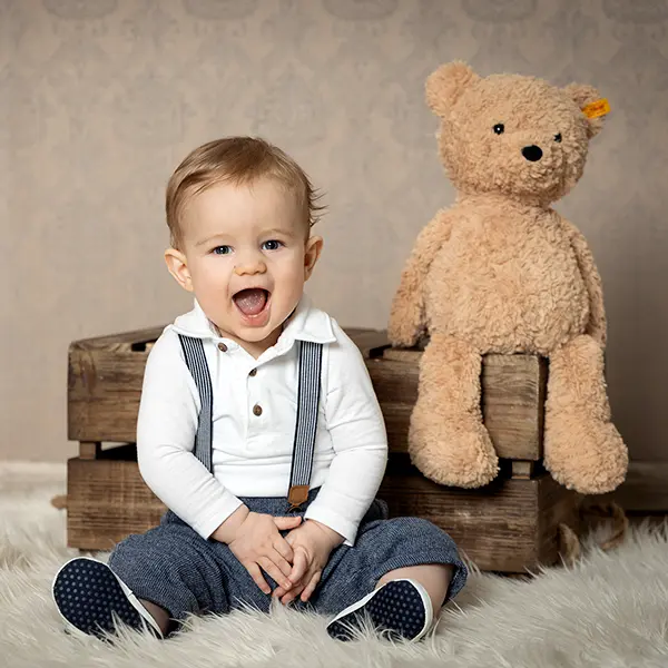 Kleinkind sitzt neben einem Teddybären bei einem liebevollen Kinderportrait im Studio