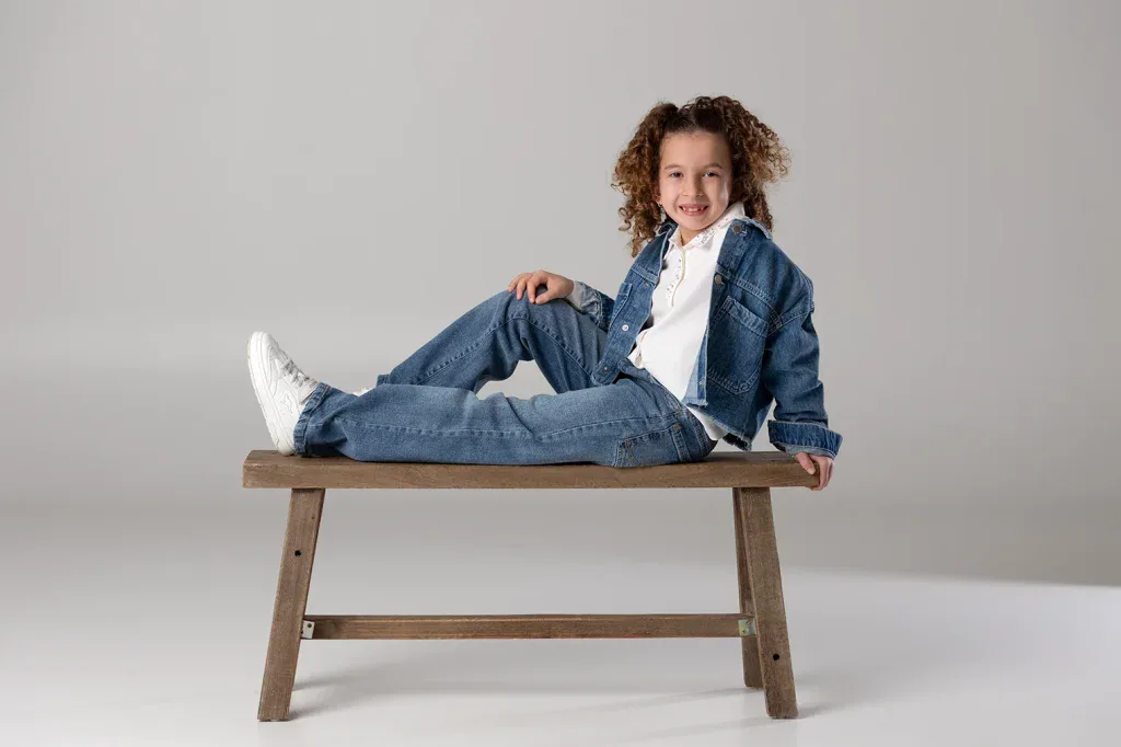 Modernes Kinderportrait in Zofingen mit Mädchen in Jeans-Outfit auf Holzbank im hellen Studio