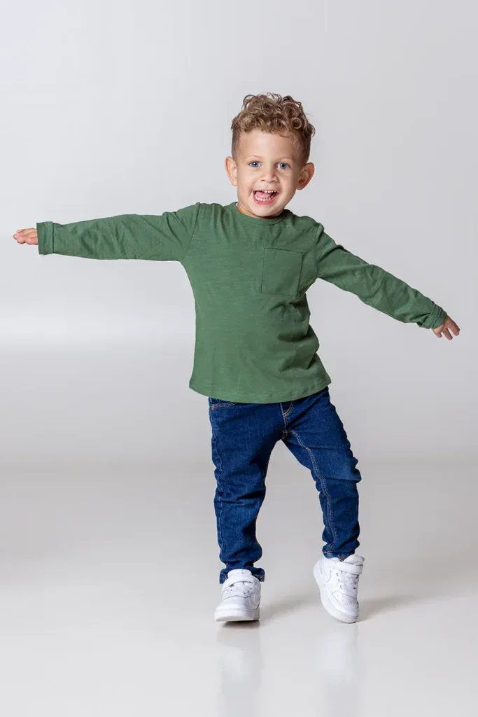 Lebendiges Kinderportrait in Zofingen mit lachendem Jungen, grüner Kleidung und natürlicher Bewegung