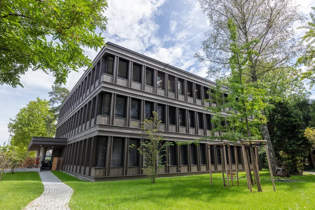 Mehrgeschossiges Bürogebäude mit dunkler Holzfassade, grossen Fenstern und umliegendem Baumbestand.