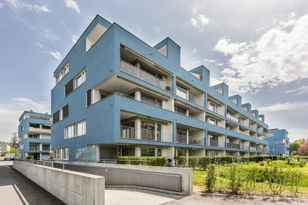 Aussenansicht eines modernen Mehrfamilienhauses mit Balkonen, Grünflächen und klarer Architektur.