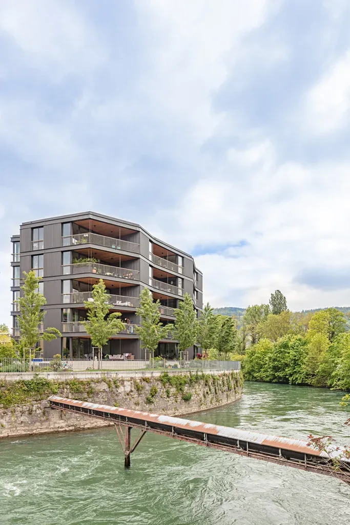 Moderne Wohngebäude der Spinnerei Windisch an einem begrünten Flussufer.