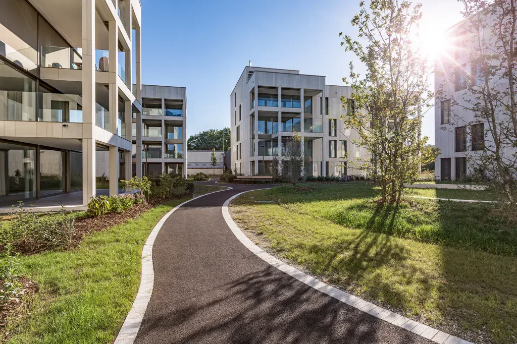 Moderne Wohnanlage mit begrüntem Innenbereich, geschwungenem Weg und mehrgeschossigen Gebäuden.
