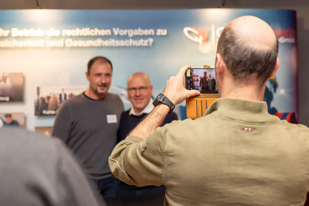 Teilnehmer fotografiert zwei Gäste mit dem Smartphone vor einer Eventwand.