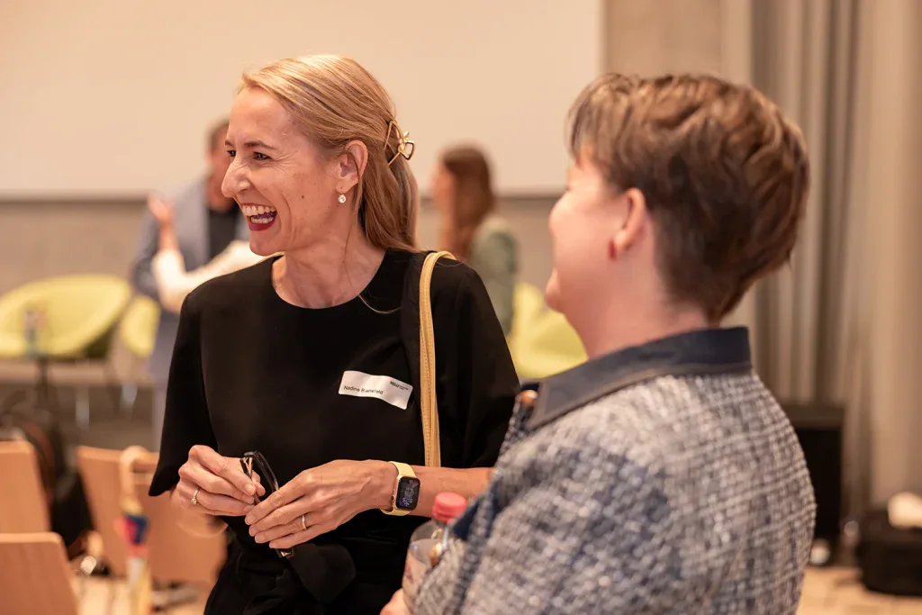 Zwei Teilnehmerinnen lachen während eines persönlichen Gesprächs an einem Business-Event.
