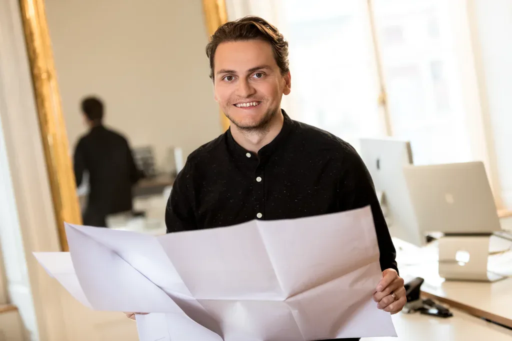 Businessportrait eines Architekten mit Plänen und Unterlagen im Büro, passend für Architekturunternehmen und Teamseiten.
