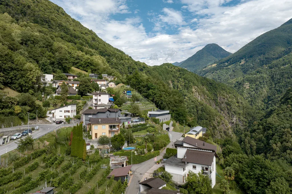 Drohnenaufnahme einer Wohnsiedlung in Pianezzo mit grüner Berglandschaft und Talblick.