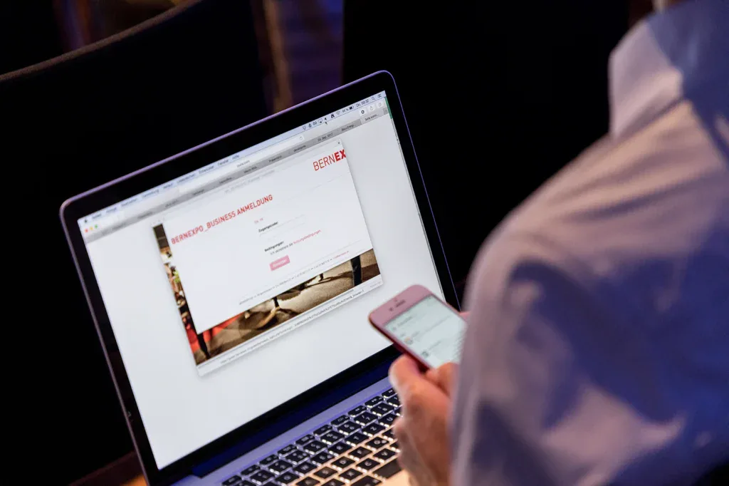 Nahaufnahme eines Teilnehmers, der sich mit Laptop und Smartphone für ein Business-Event anmeldet.