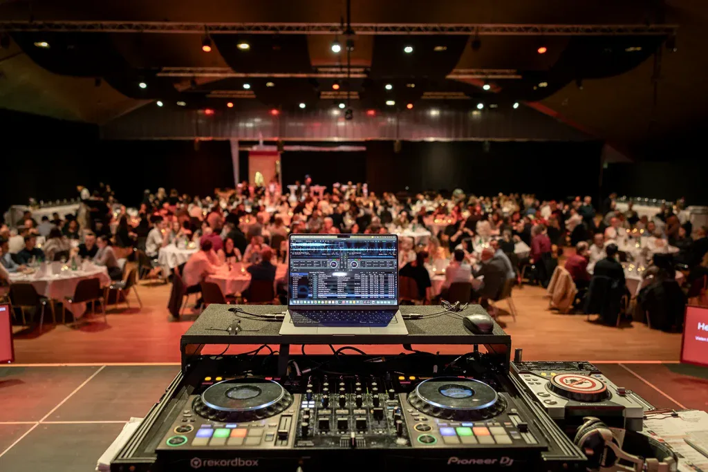 DJ-Pult im Vordergrund mit Blick auf einen voll besetzten Veranstaltungssaal.