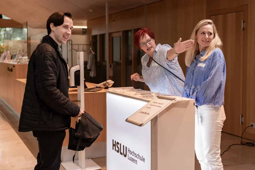 Zwei Mitarbeiterinnen begrüssen einen eintreffenden Gast am Empfang einer Veranstaltung.