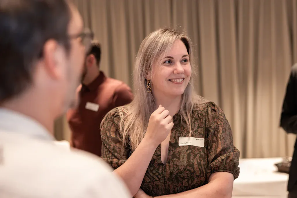 Lächelnde Teilnehmerin im Gespräch mit einem anderen Gast während eines Firmenevents.