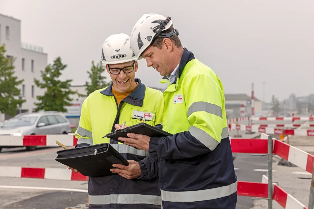 Zwei Mitarbeitende mit Schutzhelmen prüfen digitale Pläne auf einer Baustelle in Zofingen.