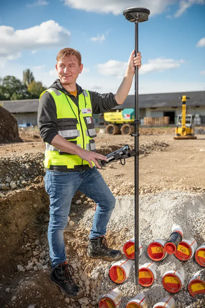 Vermessungsfachperson hält einen GPS-Messstab auf einer Baustelle in Zofingen.