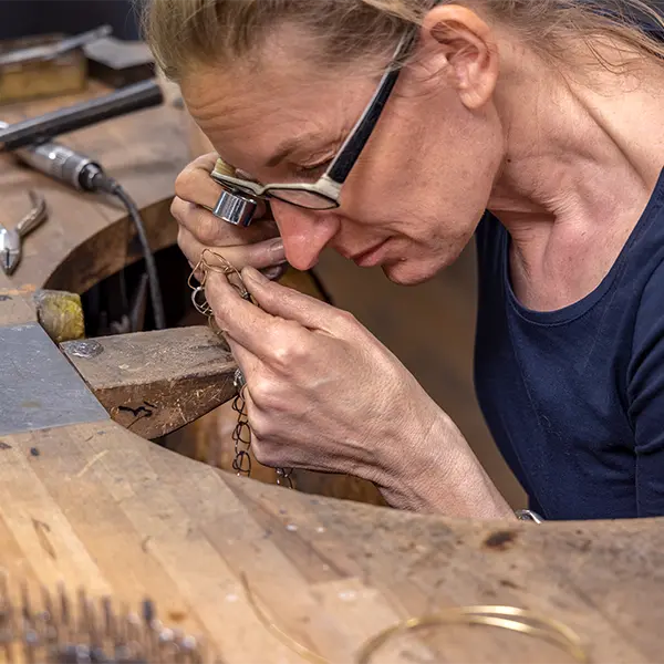 Goldschmiedin arbeitet konzentriert an einem Schmuckstück in ihrer Werkstatt.