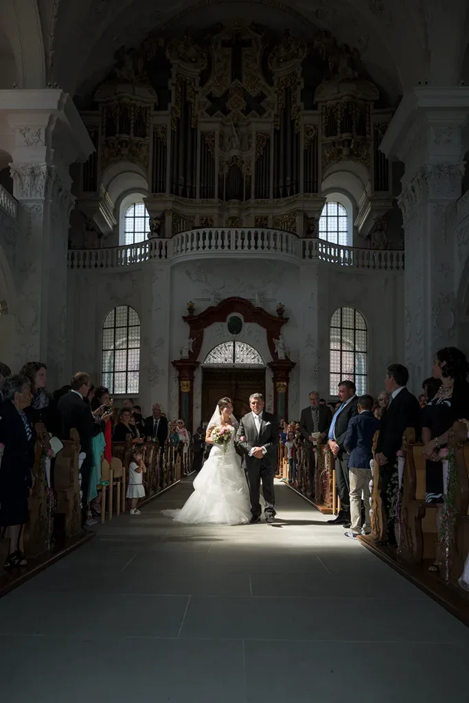 Braut beim Einzug in die Kirche mit Begleitung und Gästen während der Hochzeitszeremonie.
