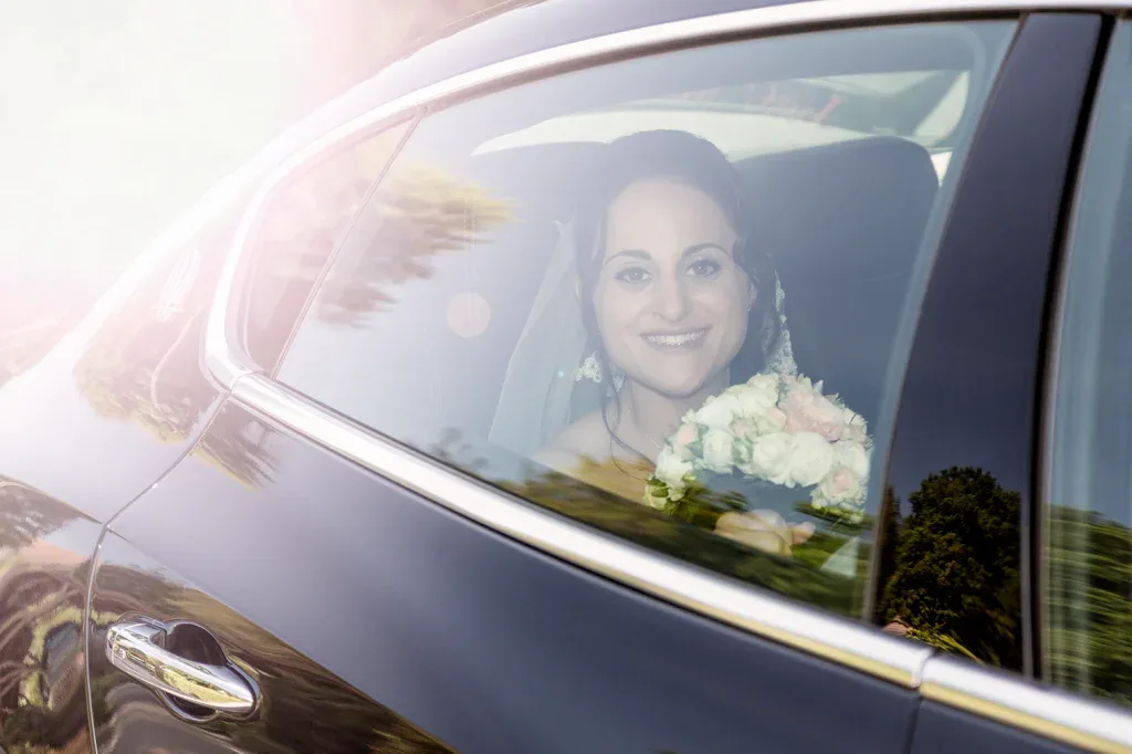 Braut mit Brautstrauss im Hochzeitsauto, fotografiert durch die Autoscheibe mit natürlichem Licht.