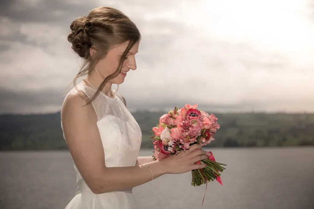 Braut mit farbigem Brautstrauss bei einem natürlichen Hochzeitsportrait am See.