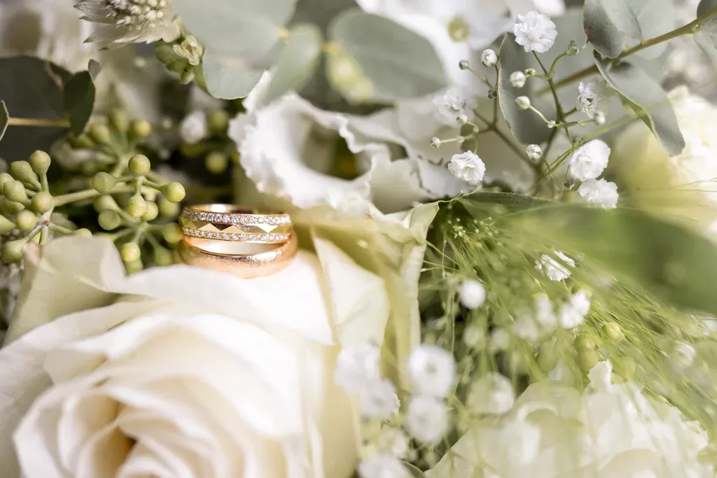 Eheringe in einem hellen Brautstrauss mit weissen Blumen als Hochzeitsdetail.
