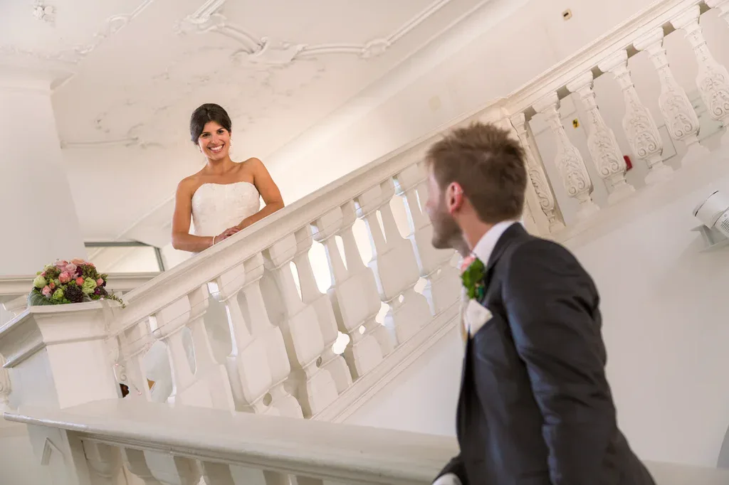 Braut und Bräutigam beim First Look auf einer hellen Treppe als Teil einer natürlichen Hochzeitsreportage.