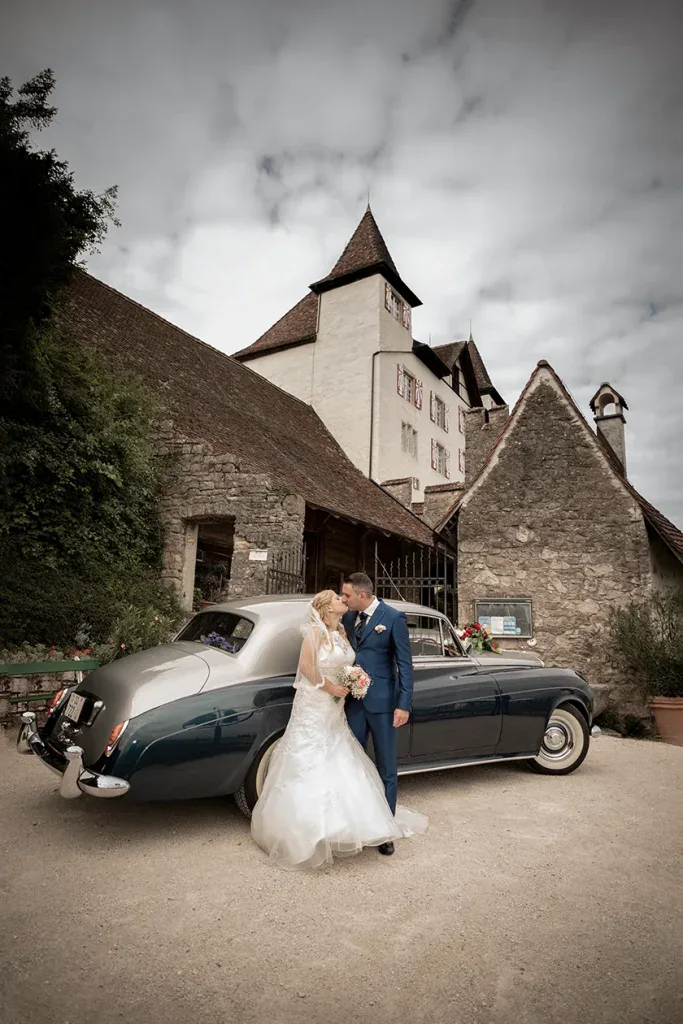 Brautpaar bei einem Hochzeitsportrait vor einem historischen Schloss mit Oldtimer.