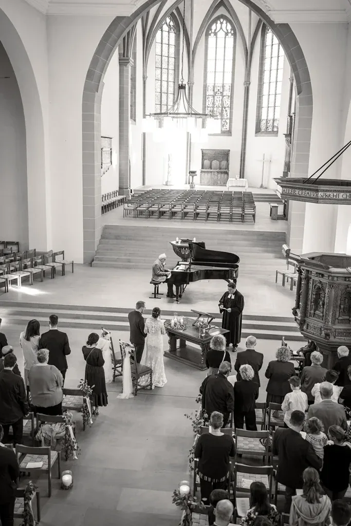 Kirchliche Hochzeitszeremonie mit Brautpaar, Gästen und Musiker in einer grossen Kirche.