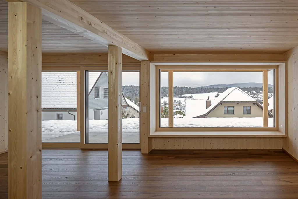 Heller Wohnraum einer Dachwohnung mit Holzdecke, grossen Fenstern und Blick über Vordemwald.