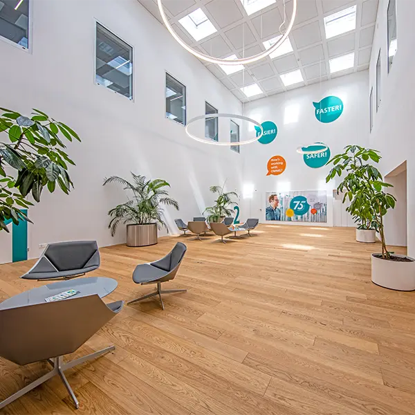 Heller Empfangsbereich mit Holzboden, Sitzgruppen, Pflanzen und offenem Atrium in einem Unternehmensgebäude.