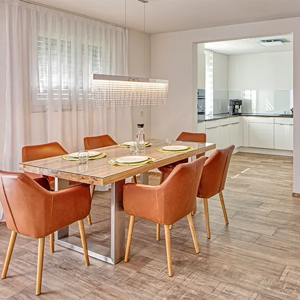 Heller Essbereich mit Esstisch, orangefarbenen Stühlen und offener Küche in einer modernen Wohnung.
