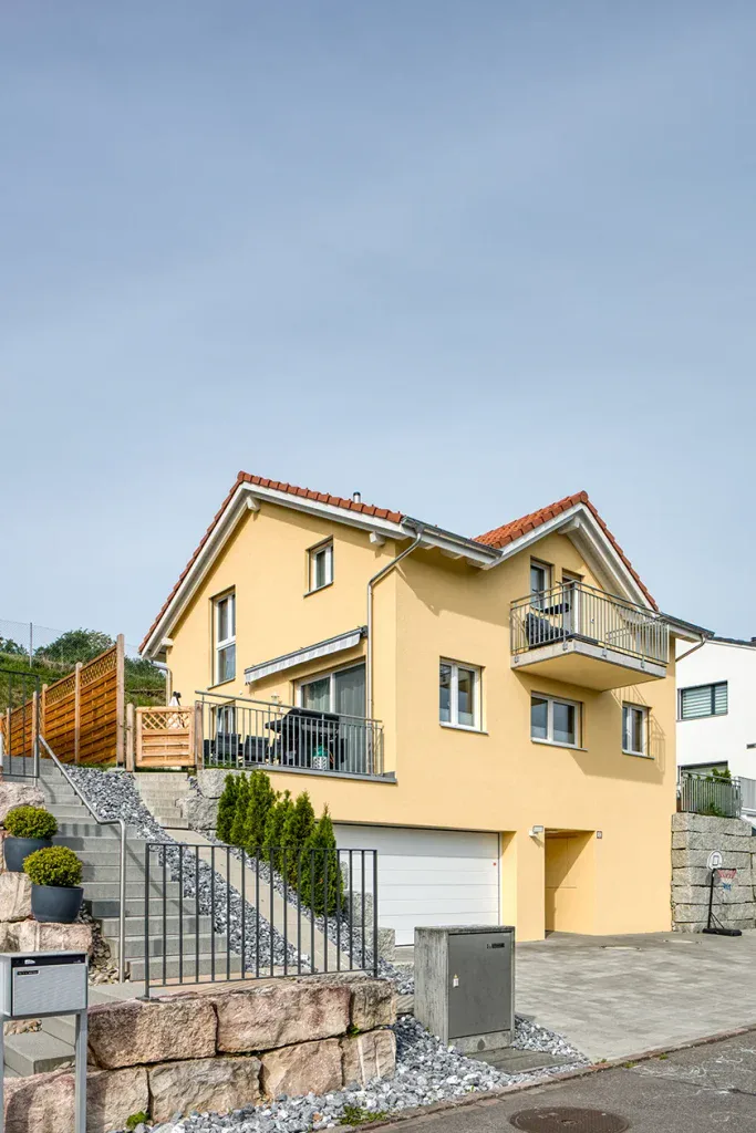 Aussenansicht eines gelben Mehrfamilienhauses mit Balkonen und gepflegtem Vorgarten.