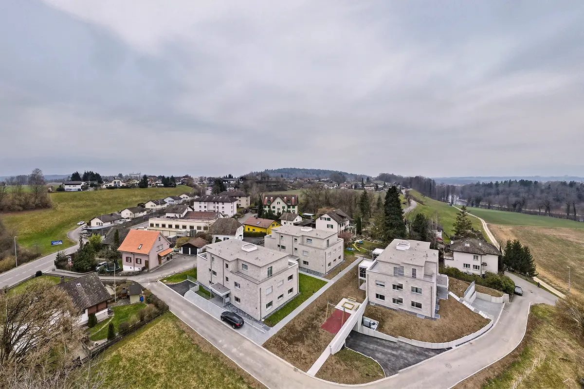 Drohnenaufnahme einer modernen Wohnüberbauung mit drei Mehrfamilienhäusern und den angrenzenden Wohnquartieren im Aargau.