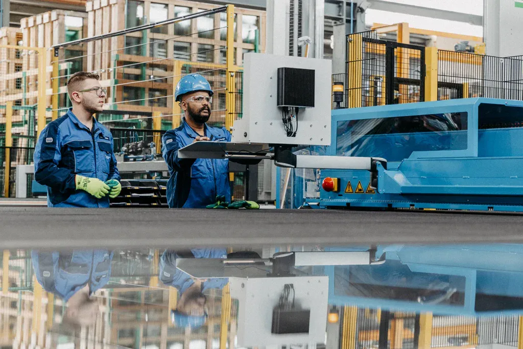 Zwei Mitarbeitende in Arbeitskleidung bedienen gemeinsam eine grosse Maschine in einem Industriebetrieb.