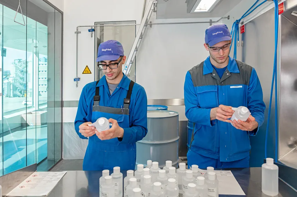 Zwei Mitarbeitende in blauer Schutzkleidung kontrollieren Kunststoffflaschen in einem Pharmaunternehmen.