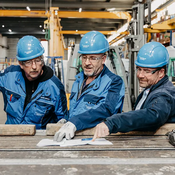 Mitarbeitende besprechen technische Pläne in einer Produktionshalle während einer Firmenreportage.