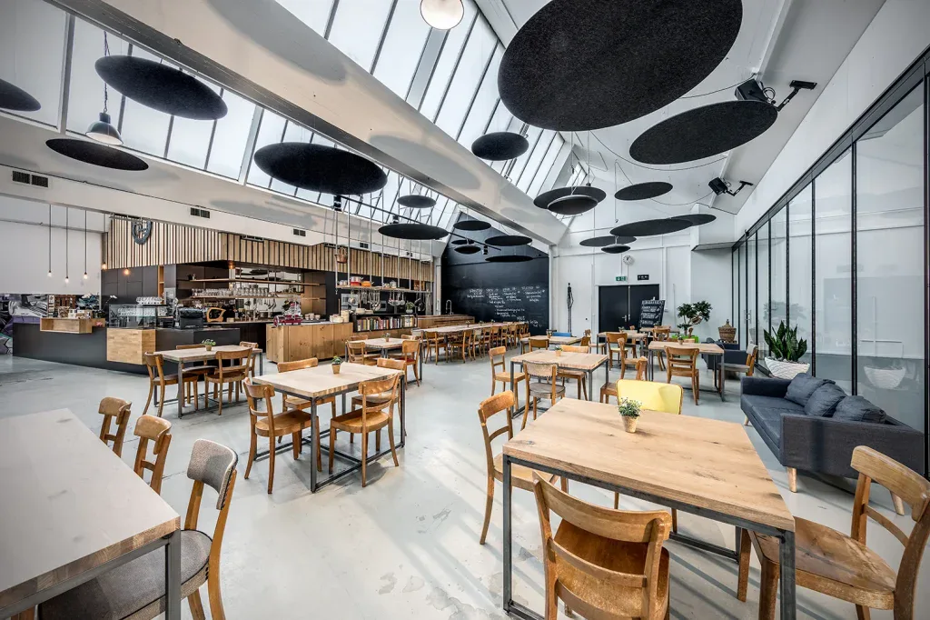 Grosszügiger Restaurantbereich mit Holzmöbeln, Oberlichtern und markanten Akustikelementen an der Decke.