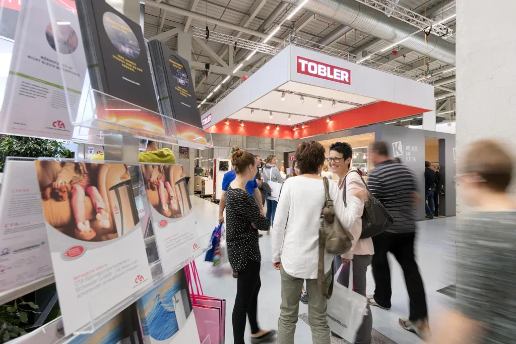 Besucherinnen und Besucher bewegen sich durch eine belebte Fachmesse mit verschiedenen Messeständen.