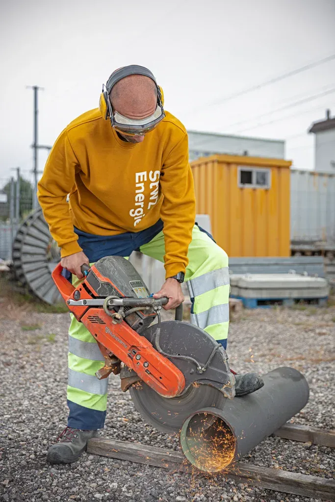 Mitarbeiter in Warnkleidung schneidet auf einer Baustelle ein Rohr mit einem Trennschleifer.