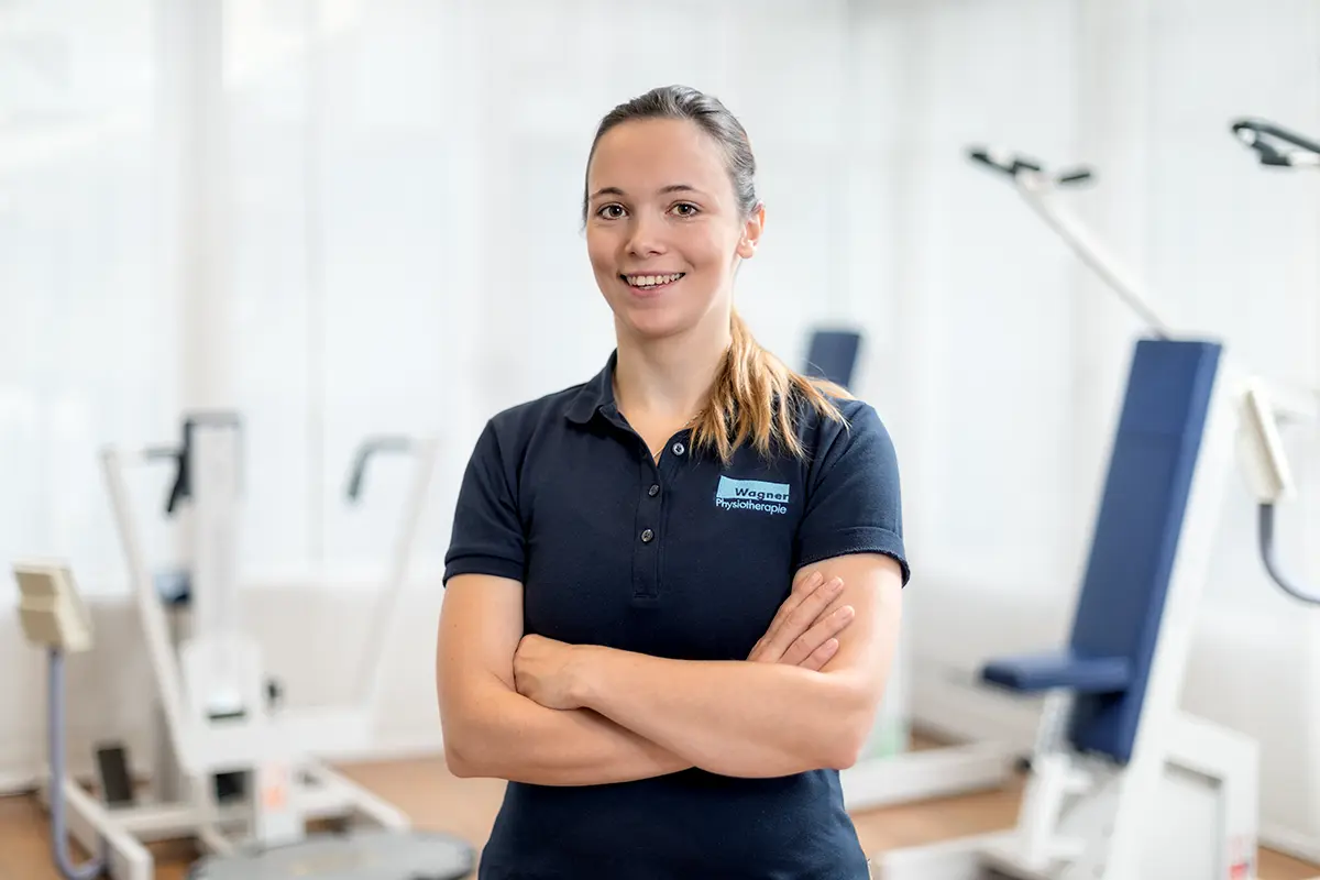 Freundliches Mitarbeiterportrait einer Physiotherapeutin in einem hellen Behandlungsraum.