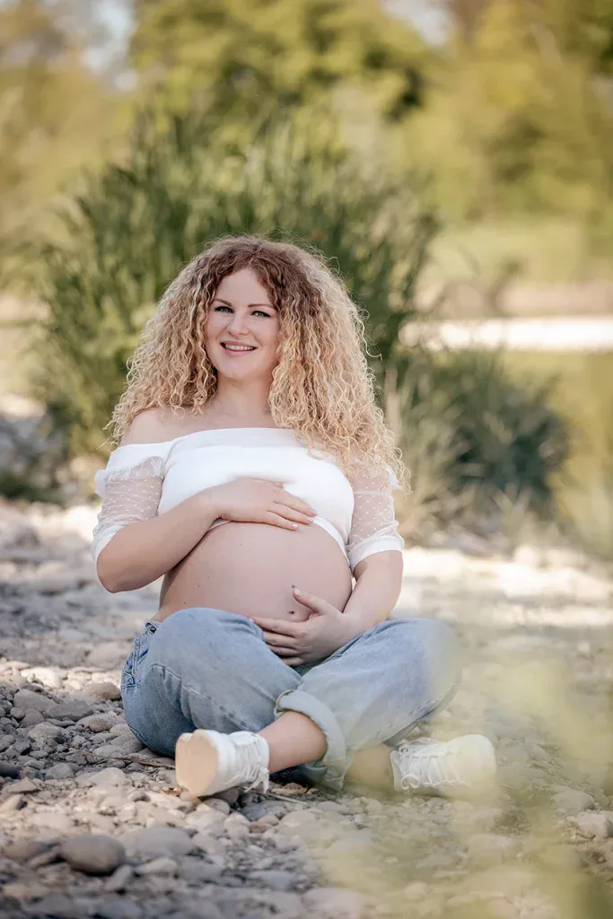 Schwangere Frau bei einem natürlichen Outdoor-Babybauchshooting in ruhiger Umgebung.