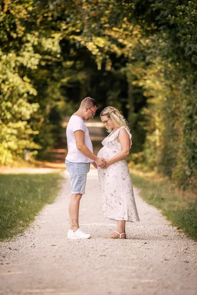 Werdende Eltern bei einem natürlichen Babybauchshooting draussen auf einem Waldweg.