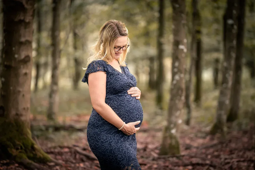 Schwangere Frau bei einem Babybauch-Fotoshooting draussen im Wald mit natürlicher Lichtstimmung.