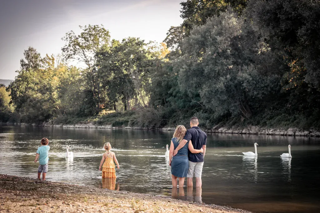 Familie bei einem natürlichen Outdoor-Fotoshooting am Wasser mit Kindern und Schwänen.