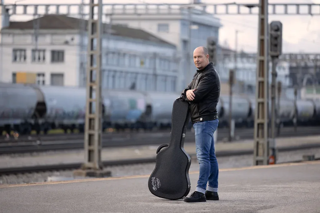 Musiker mit Gitarrenkoffer bei einem Outdoor-Portraitshooting an einer urbanen Location.