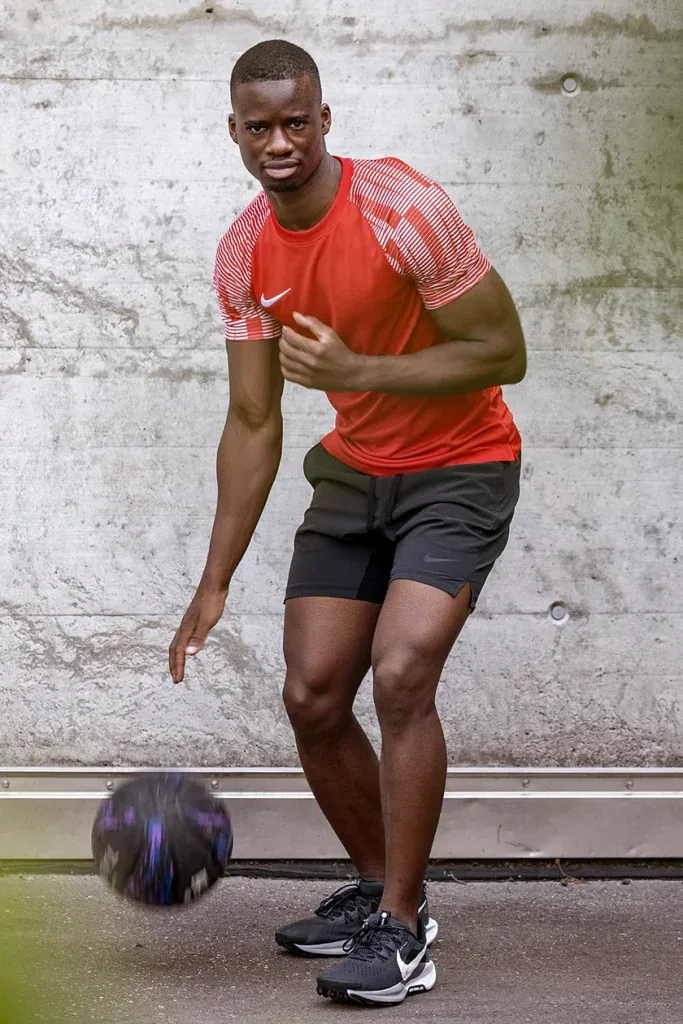 Sportler bei einem dynamischen Outdoor-Sportportrait mit Basketball vor einer Betonwand.