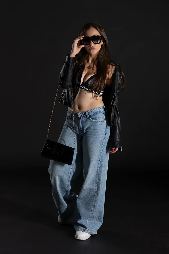 Modernes Fashionportrait in Zofingen mit Frau, Sonnenbrille und Lederjacke vor dunklem Studiohintergrund.