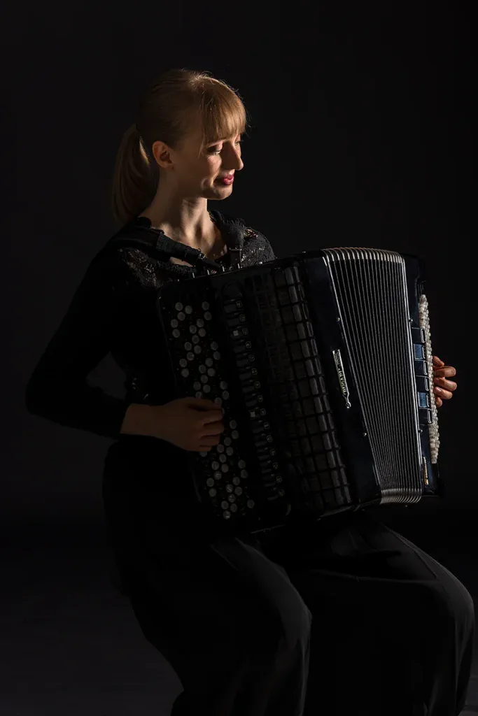 Künstlerisches Portraitshooting in Zofingen mit Musikerin und Akkordeon vor dunklem Studiohintergrund.
