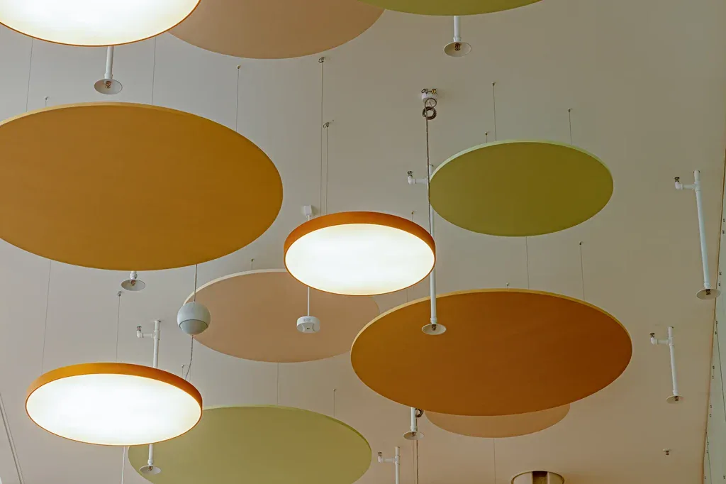 Mehrere runde Akustik- und Leuchtenelemente in Gelb, Orange und Grün an einer Decke in Kriens.