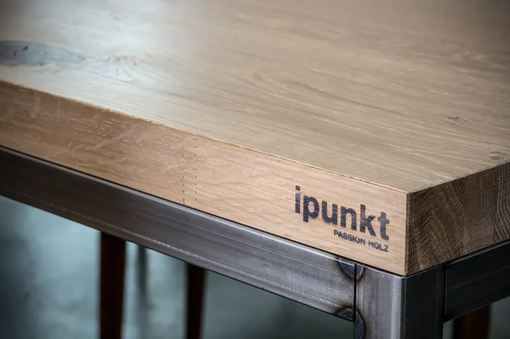 Detailaufnahme einer massiven Holztischkante mit eingearbeitetem Markenlogo.
