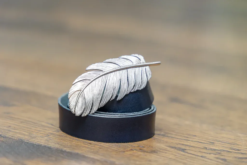 Silberne Brosche in Federform auf schwarzem Sockel als hochwertige Schmuckaufnahme.